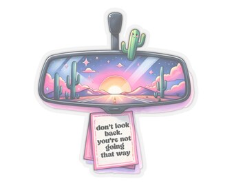 May include: A pink and blue car rearview mirror with a cactus and a sunset reflected in it. A pink note attached to the mirror reads "don't look back. you're not going that way."