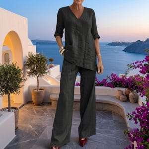 May include: A dark charcoal gray two-piece set consisting of a V-neck tunic top with three-quarter length sleeves and matching wide-leg trousers. The top features a slightly asymmetrical hemline, and the trousers have a relaxed, loose fit.