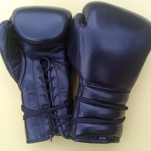 May include: A pair of black boxing gloves featuring a lace-up closure system on the front of one glove and a smooth, padded surface on the other. The gloves are marked with the text 14 oz on the wrist area, indicating their weight in ounces.
