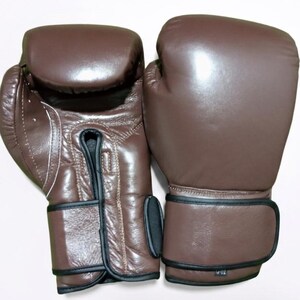 May include: A pair of brown boxing gloves featuring a smooth, solid-colored exterior with black trim along the wrist straps and seams. The gloves have a padded knuckle area and a secure hook-and-loop closure system on the wrist for support.