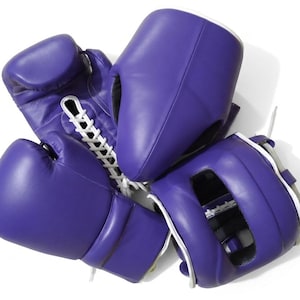 May include: A set of purple boxing equipment consisting of two lace-up boxing gloves and a protective headgear piece. The gloves feature white laces and smooth purple surfaces, while the headgear has a matching purple exterior and white trim.
