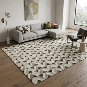 Peut inclure: Un grand tapis rectangulaire présentant un motif géométrique répétitif dans des tons crème, gris et noir. Le tapis est composé de petites pièces angulaires disposées en chevrons, couvrant une partie importante du plancher en bois.