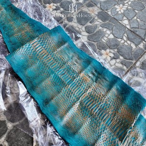 May include: A teal and gold python skin hide featuring a distinct scale pattern and a natural texture. The leather is partially wrapped in clear plastic packaging and displays the logo and text GoPythonHouse at the top center of the image.