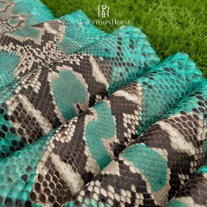 May include: A piece of genuine python skin leather featuring a vibrant turquoise and black diamond-shaped scale pattern. The material is folded in layers, showcasing the natural texture and repeating geometric design with the text GoPythonHouse.