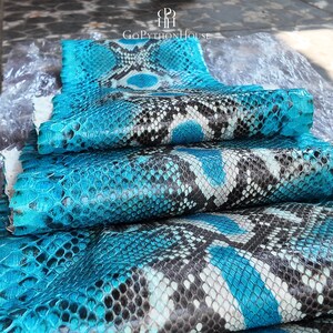 May include: A folded sheet of genuine python skin featuring a vibrant turquoise and black diamond-shaped scale pattern. The material displays a natural, textured surface with a glossy finish. The text GoPythonHouse is visible at the top center.