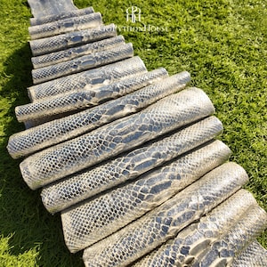 May include: A series of metallic silver python skin rolls arranged in a cascading pattern. Each roll displays a distinct, textured scale pattern characteristic of snakeskin. The logo for GoPythonHouse is visible at the top of the arrangement.