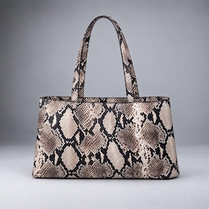 Puede incluir: Un bolso tote estructurado con un llamativo estampado de piel de serpiente en tonos beige, marrón y negro. El bolso cuenta con dos asas superiores a juego y una base rectangular ancha, mostrando una textura detallada de escamas de reptil.