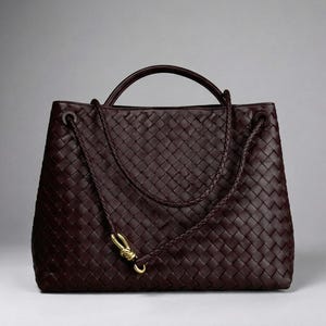 Può includere: Una borsa tote in pelle color bordeaux scuro caratterizzata da un intricato motivo intrecciato su tutto l'esterno. La borsa include un singolo manico superiore arrotondato e una lunga tracolla sottile intrecciata con una chiusura in metallo dorato.