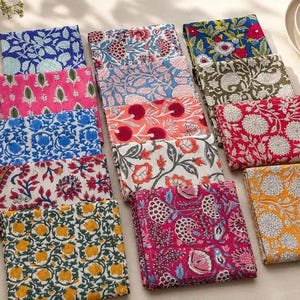 Puede incluir: Una colección de servilletas de tela cuadradas con una variedad de coloridos estampados florales y botánicos en tonos azul, rosa, rojo, amarillo y verde, dispuestas en una cuadrícula ordenada sobre una superficie de color neutro.