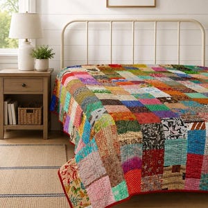 Puede incluir: Una colcha de patchwork que presenta una cuadrícula de cuadrados de tela multicolores con varios patrones, incluyendo estampados florales, geométricos y abstractos. La colcha tiene costuras visibles y un borde de tela rojo sólido.
