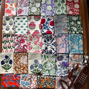 Puede incluir: Una colección de treinta y cuatro muestras de tela rectangulares con diversos patrones florales y botánicos estampados en bloque en varios colores, incluyendo rojo, azul, verde, naranja y morado, dispuestos en una cuadrícula.