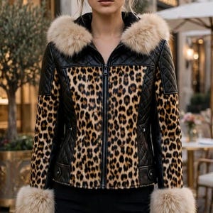 May include: A black quilted jacket featuring a central leopard print panel, a hood with beige faux fur trim, and matching beige faux fur cuffs on the long sleeves. The jacket has a full-length front zip closure and black trousers.