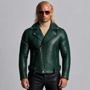 May include: A dark green motorcycle jacket featuring a textured snakeskin pattern, a wide notched lapel, silver-toned metal hardware, an asymmetrical front zipper closure, and an adjustable buckled belt at the waist, worn over a beige turtleneck.