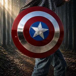 May include: A red, silver, and blue shield with a white star in the center. The shield is round with a red outer ring, a silver middle ring, and a blue center. The shield is held in front of a person in a forest.
