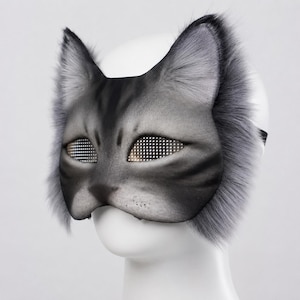 以下が含まれることがあります： リアルなデザインのグレーの猫のマスク。詳細な顔、耳、毛皮のトリムが特徴です。目はメッシュ素材で作られています。マスクは顔に着用するように設計されています。