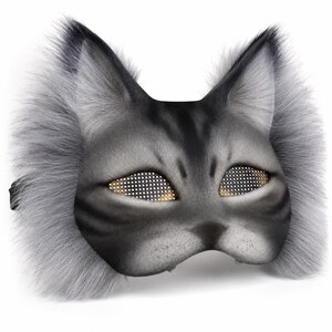 May include: A gray cat mask with a faux fur trim and detailed facial features. The eyes are designed with a grid of small, gold-colored dots. The mask has a black strap for securing it.
