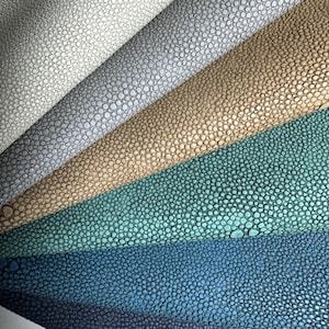 May include: A selection of textured leather samples in a fan arrangement. The colours range from light grey to navy, including grey, tan, teal, and blue. The leather has a distinctive bumpy texture, with small, closely packed, circular bumps.