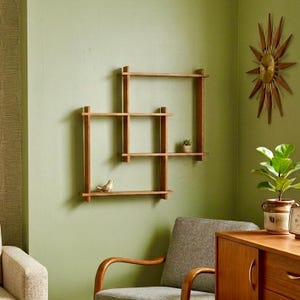May include: A wall-mounted wooden shelving unit with an interlocking square design. The shelves feature a natural wood grain finish and hold a small decorative bird figurine and a tiny potted succulent plant on the horizontal surfaces.