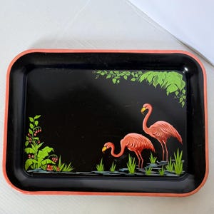 May include: A rectangular serving tray with a black base and a coral-colored rim. The tray features a painted illustration of two pink flamingos standing in water, surrounded by green foliage and small red berries on a black background.