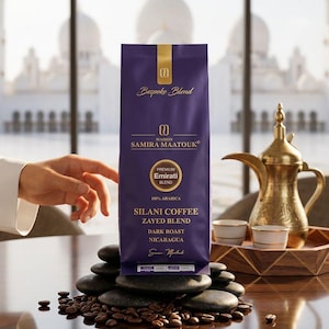 Puede incluir: Una bolsa morada de café Maison Samira Maatouk Silani Coffee Zayed Blend, con texto y marca en dorado. La etiqueta especifica Premium Emirati Blend, 100% Arabica, Dark Roast y Nicaragua. La bolsa descansa sobre piedras negras lisas.