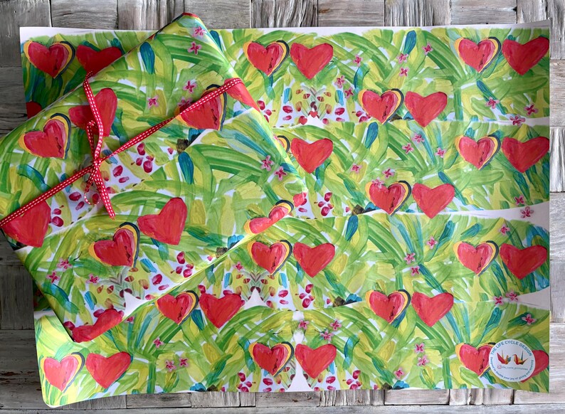 May include: Gift wrap featuring a vibrant pattern of red hearts and green foliage. The paper is tied with a red and white polka dot ribbon. The design includes small pink floral accents, creating a cheerful and festive look.