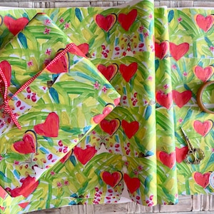 May include: Gift wrap with a vibrant watercolor design featuring red hearts and green foliage on a yellow background. A wrapped gift is tied with a red ribbon. A roll of tape and small gold scissors are also visible.