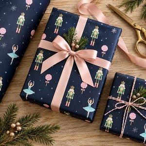 May include: Dark navy blue wrapping paper featuring a repeating pattern of nutcrackers, ballerinas, pink swirl lollipops, and white snowflakes. Two rectangular gifts are wrapped in this paper, one with a pink satin ribbon bow and one with red and white twine.