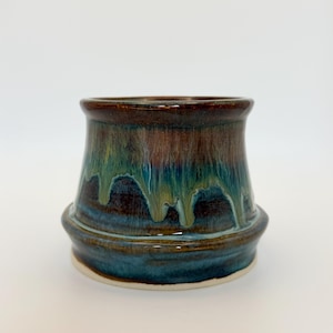 May include: A ceramic planter with a wide, flared rim and a tapered body. The glaze features a deep brown base color with vertical drips of teal and light green running down the sides, creating a layered, multi-toned appearance.