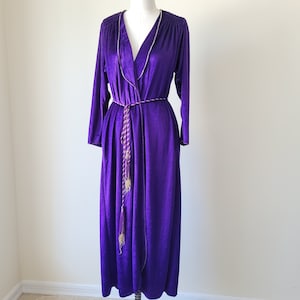 May include: A long purple robe with a gold and purple trim and a matching sash. The robe has a V-neck and long sleeves.
