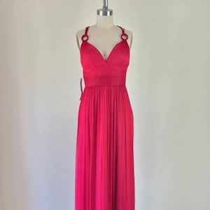 May include: A long, bright pink, sleeveless maxi dress with a V-neckline and a gathered skirt. The dress has thin straps with decorative rings at the shoulders.