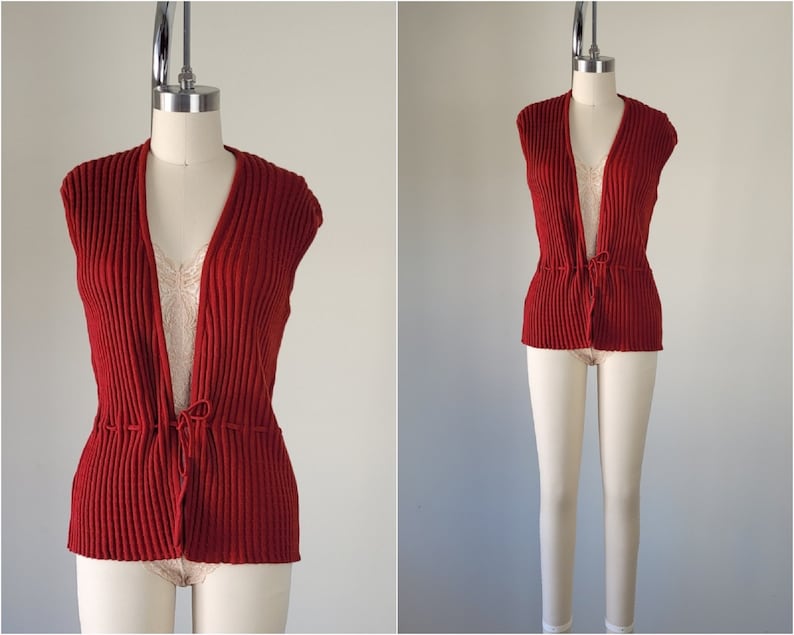 May include: A red knitted sleeveless vest with a tie at the waist.