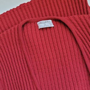 May include: A red ribbed knit cardigan with a V-neck. The label reads "Jaeger" and includes information about the material and care instructions.