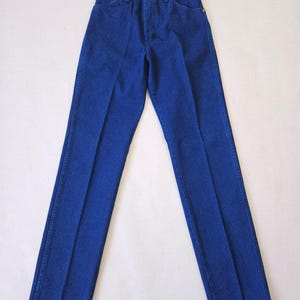 May include: A pair of classic blue denim jeans. The jeans have a straight leg cut, a button and zipper closure, and pockets. The denim is a solid, medium blue color. The jeans are laid flat on a white surface.