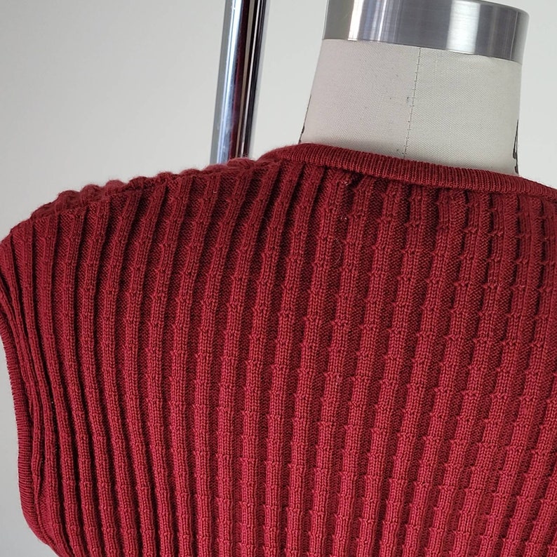 May include: A close-up of a red ribbed knit sweater. The sweater has a round neckline and a smooth texture.