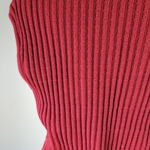 May include: A close-up of a red ribbed knit fabric. The fabric has a fine knit and a smooth texture.