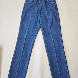May include: Classic blue denim jeans with a straight leg cut. The jeans feature a button and zipper closure, front and back pockets, and belt loops. The denim has a medium wash and a traditional five-pocket design.