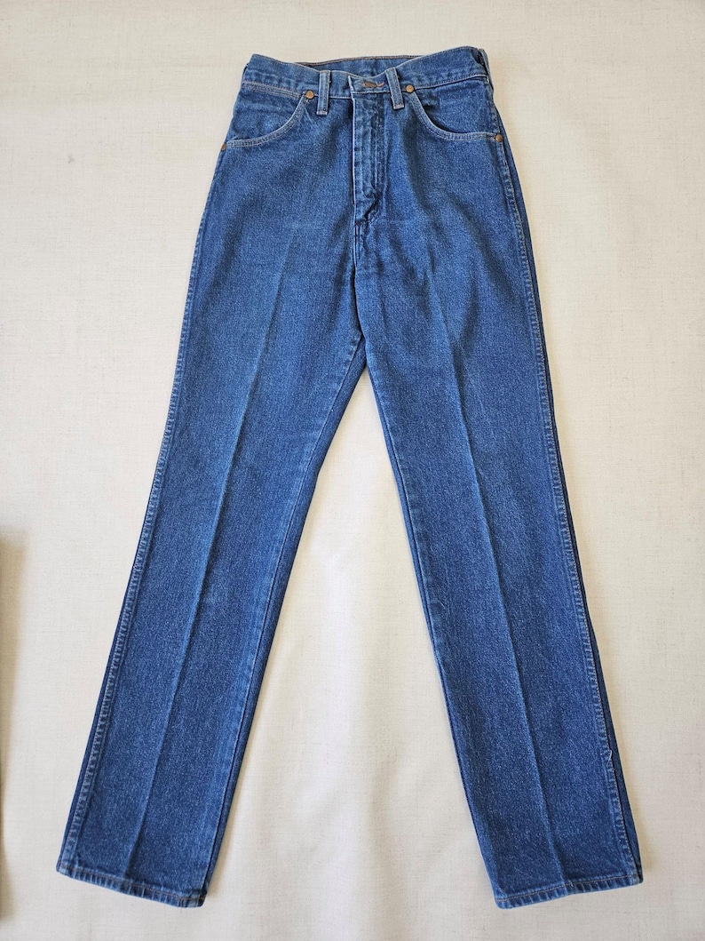 May include: Classic blue denim jeans with a straight leg cut. The jeans feature a button and zipper closure, front and back pockets, and belt loops. The denim has a medium wash and a traditional five-pocket design.