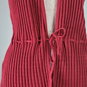 May include: A close-up of a red ribbed knit cardigan with a tie closure at the front.