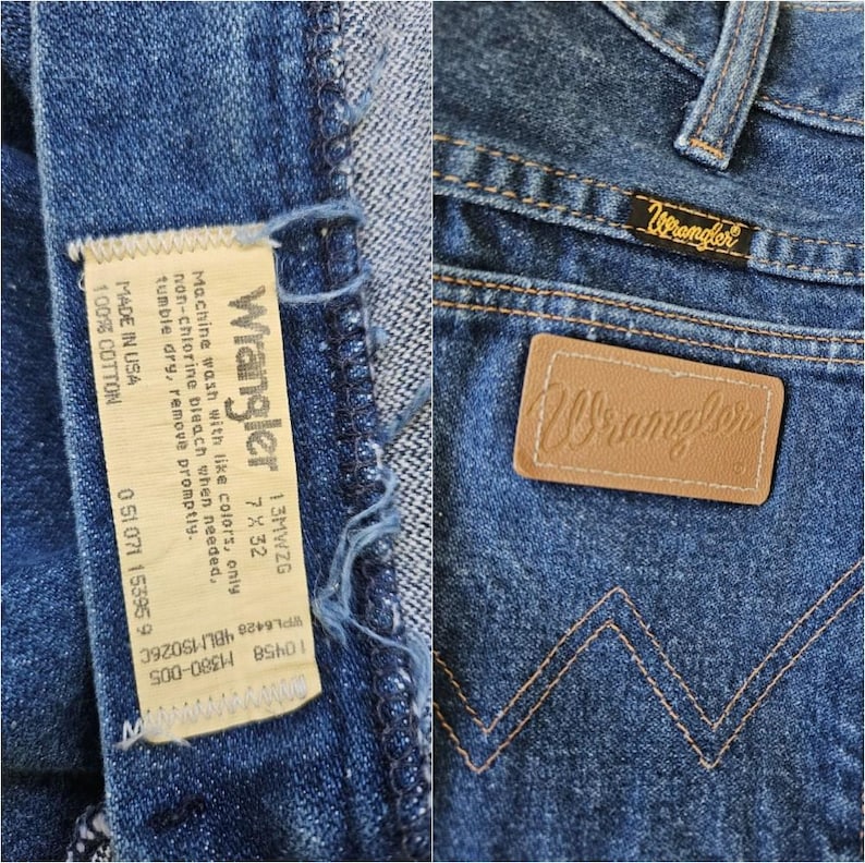 May include: Close-up of blue denim Wrangler jeans. The jeans feature a leather patch with the Wrangler logo, a small tag with the Wrangler brand name, and a care label. The jeans are made of 100% cotton.