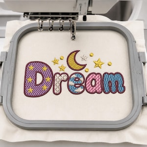 Könnte beinhalten: Ein Stickrahmen mit cremefarbenem Stoff, auf dem das Wort Dream mit farbigem Garn gestickt ist. Die Buchstaben zeigen violette, beige, blaue und rosa Muster mit gelben Sternen. Ein gelber Halbmond und kleine Sterne sind über dem Text eingestickt.