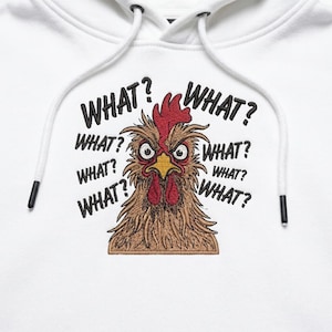Könnte beinhalten: Ein weißer Kapuzenpullover mit einer Stickerei eines braunen Huhns mit rotem Kamm und Kehllappen, großen Augen und einem gelben Schnabel. Das Wort WHAT? ist mehrfach in schwarzem Garn bogenförmig um den Kopf des Huhns gestickt.