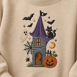 Könnte beinhalten: Ein beigefarbenes Sweatshirt mit einer gestickten Halloween-Szene, bestehend aus einem grauen Steinturm, einem violetten Dach, einer schwarzen Katze, einem Geist, einem Spinnennetz, einer Spinne, Fledermäusen, einer Mondsichel, Sternen und einem orangefarbenen Kürbis.