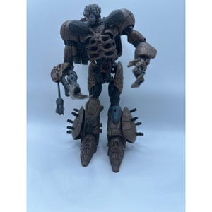 Op de afbeelding: Een bruine en zwarte gearticuleerde robotactiefiguur met een skeletachtig borstontwerp, getextureerde bepantsering en meerdere kleine uitstekende stekels op de onderbenen. Het figuur heeft een gedetailleerde kop en een wapenaccessoire.