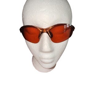 May include: Protective eyewear featuring a translucent amber-colored frame and matching orange-tinted lenses. The glasses have a wraparound design with a single-piece bridge and contoured temples, providing full coverage for the eyes and upper face area.