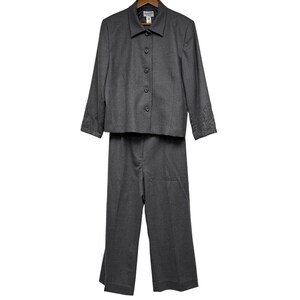 May include: A charcoal gray two-piece suit consisting of a long-sleeved button-down jacket and matching trousers. The jacket features a pointed collar, four front buttons, and subtle tonal embroidery detailing on the cuffs of both sleeves.