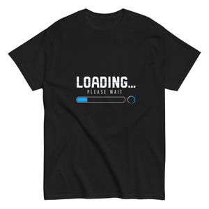 May include: A black short-sleeved t-shirt featuring a graphic print on the chest. The design displays the white text LOADING... followed by the smaller text PLEASE WAIT, positioned above a horizontal loading bar with a blue progress indicator.