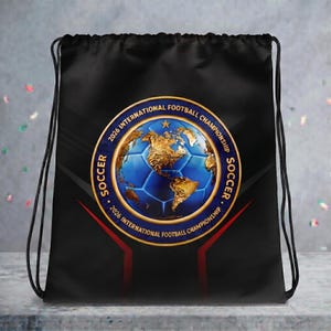 Könnte beinhalten: Ein schwarzer Rucksack mit Kordelzug und einem kreisförmigen Emblem, das einen blauen Fußball und eine goldene Karte von Nordamerika zeigt. Der Text 2026 INTERNATIONAL FOOTBALL CHAMPIONSHIP SOCCER ist in Gold um den Rand des Motivs gedruckt.