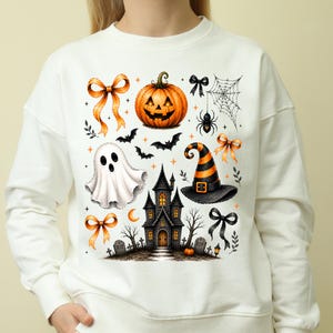 Pode incluir: Uma camisola de gola redonda cor de creme com uma impressão gráfica colorida com o tema de Halloween. O design inclui uma abóbora de Halloween, um fantasma branco, um chapéu de bruxa às riscas laranjas e pretas, uma casa assombrada, morcegos.