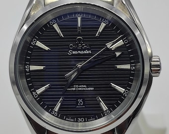 May include: A silver-toned stainless steel Omega Seamaster wristwatch with a black dial featuring horizontal lines, luminous hour markers, a date window at the six o'clock position, and the text Omega Seamaster Co-Axial Master Chronometer.