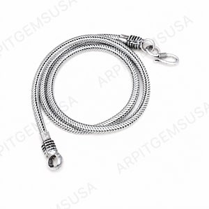 May include: A silver-toned snake chain necklace featuring a flexible, tightly woven metal link design. The necklace includes a decorative cylindrical end cap with textured detailing and a hook-style clasp mechanism for secure fastening.